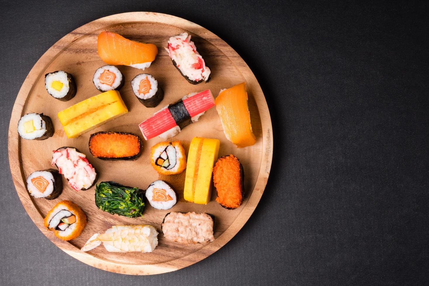 vista superior del sushi en placa de madera sobre fondo negro, comida japonesa. espacio libre para texto foto