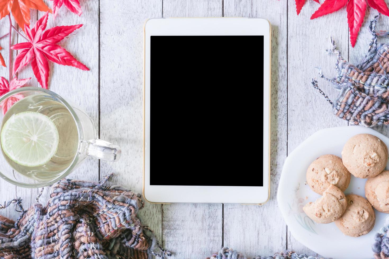 Tablet, cup of tea with lemon, cookie, scarf and maple leaves on wooden table. photo