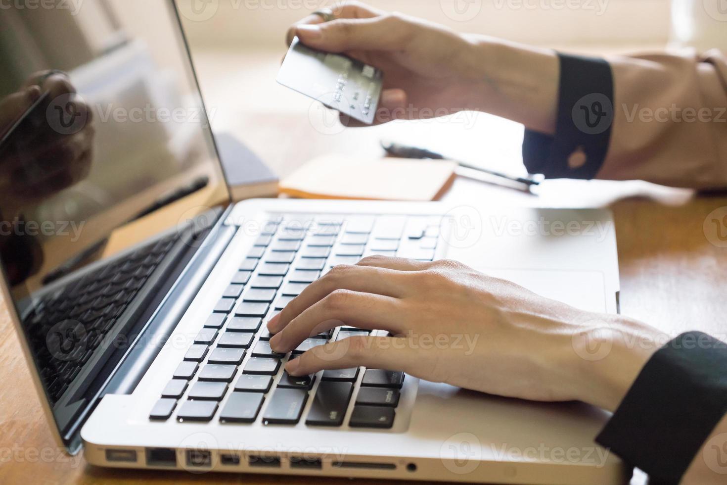 primer plano de la mano femenina que sostiene la tarjeta de crédito y usa la computadora portátil en el escritorio foto