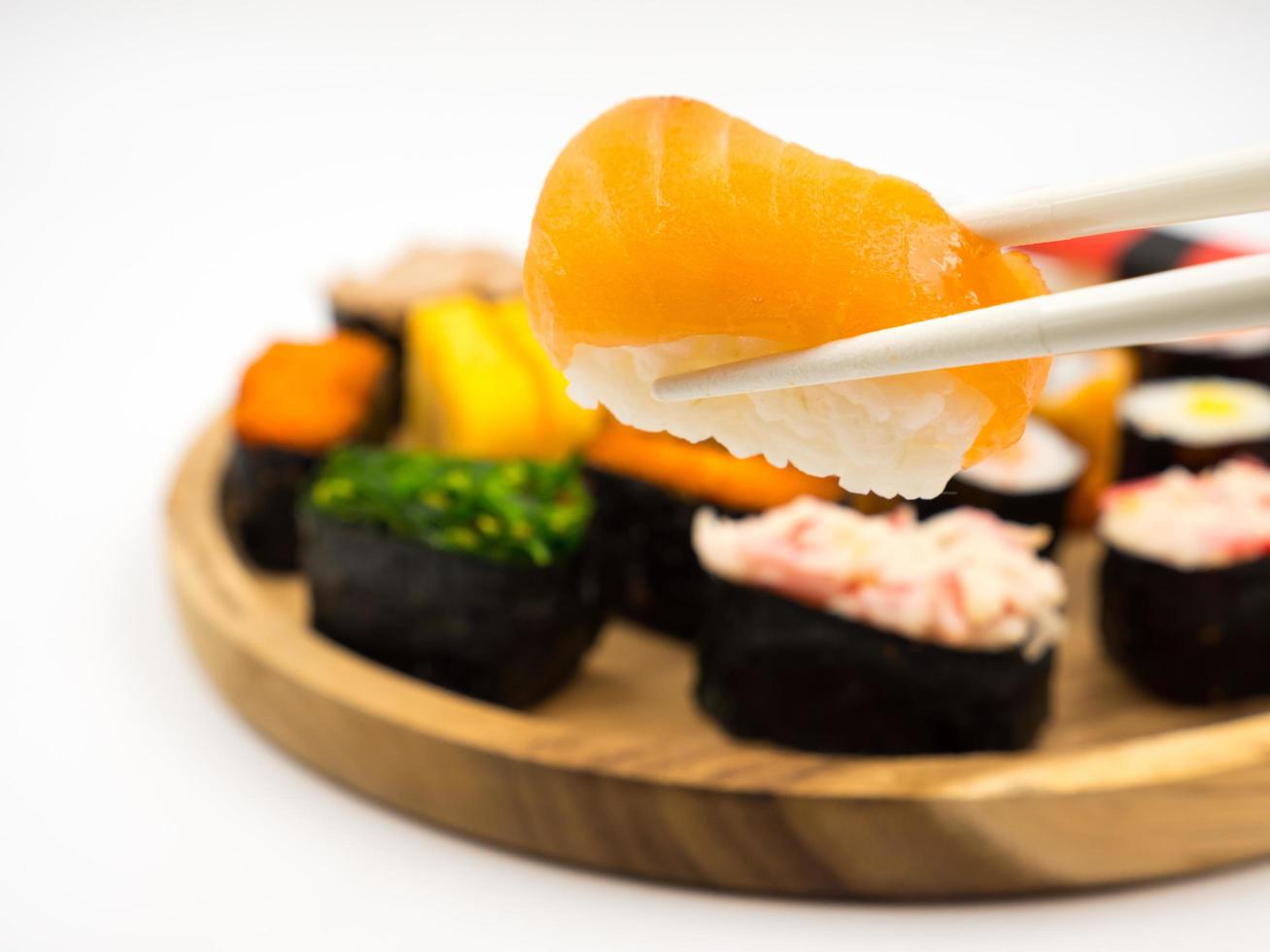 mano sosteniendo sushi con palillos, sushi sobre fondo de placa de madera, comida japonesa. foto