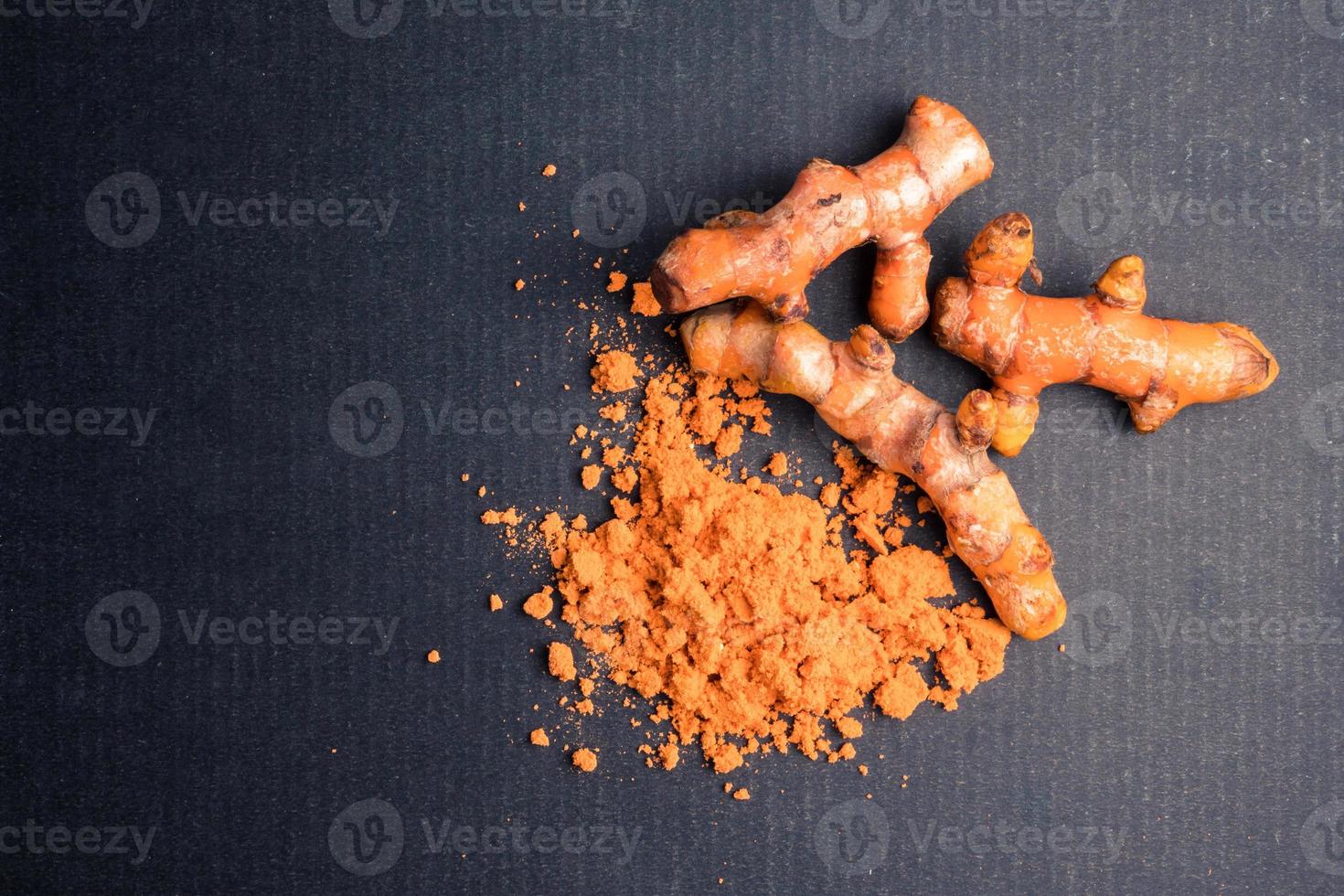 Turmeric roots with turmeric powder on black background. photo
