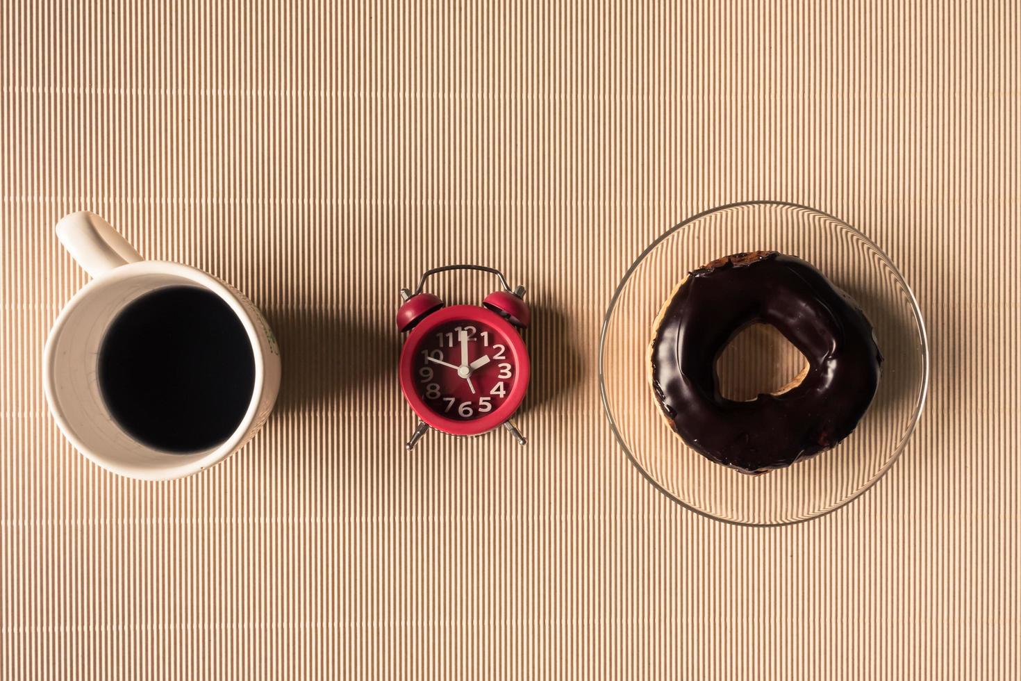 Top view of coffee cup with donut and clock on table. photo