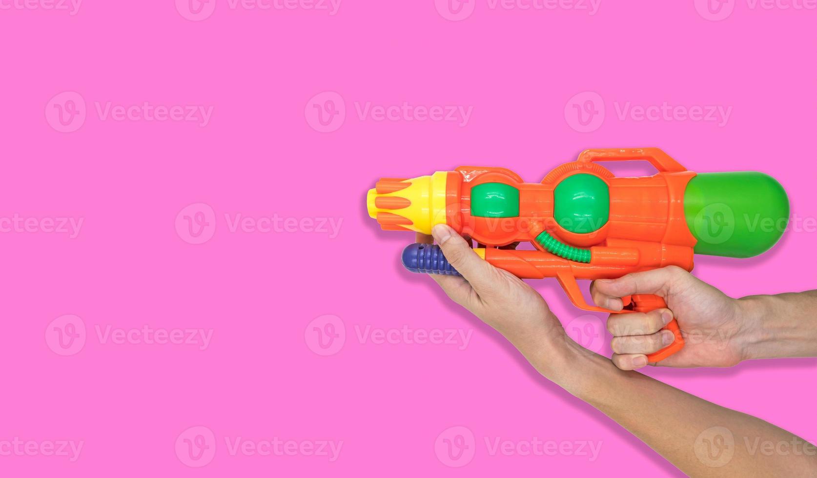 mano que sostiene el juguete de agua de pistola sobre fondo rosa. espacio libre para texto foto
