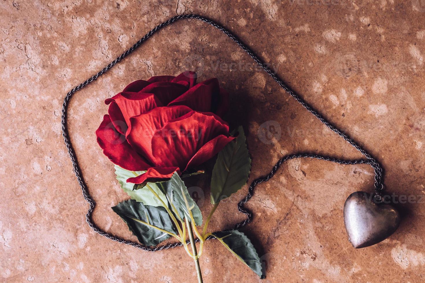 Red rose with silver heart necklace on brown grunge board background. Concept of Valentine Day. photo