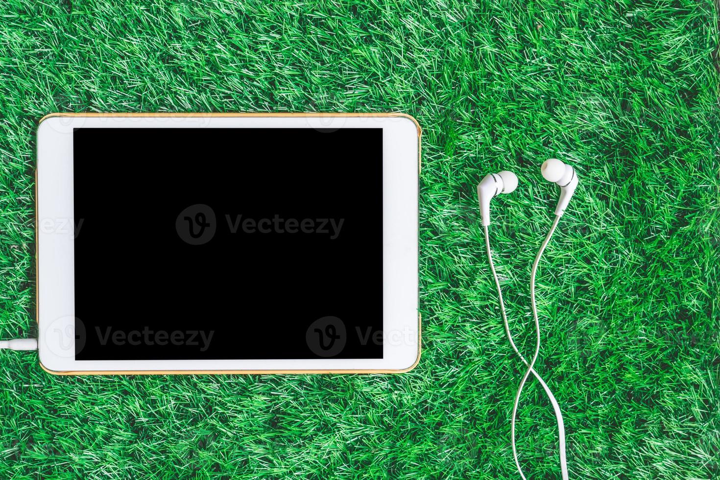 Top view of blank digital tablet with earphones on green grass background. photo