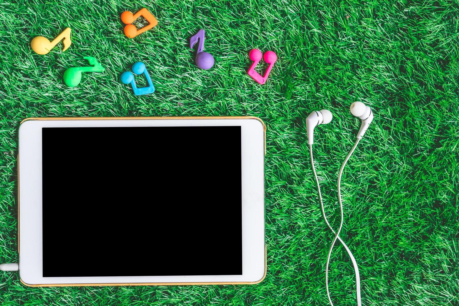 Top view of blank digital tablet with earphones on green grass background. photo