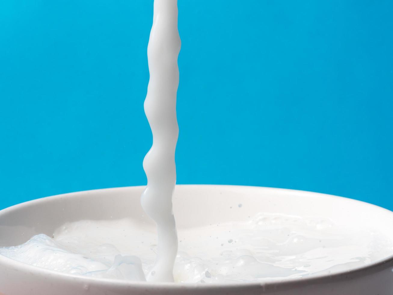 Splash of milk from a cup on blue background. photo