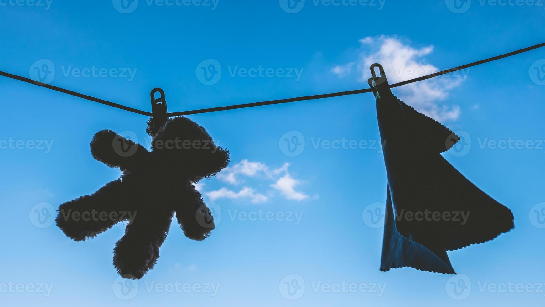 Silhouette of Teddy bear and napkin hanging on the clothes line with blue sky. photo