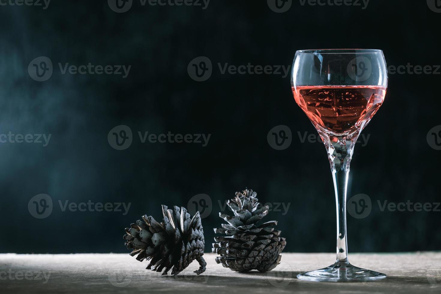 Glass of wine with pine cones on the wooden table, black background, free space for text photo