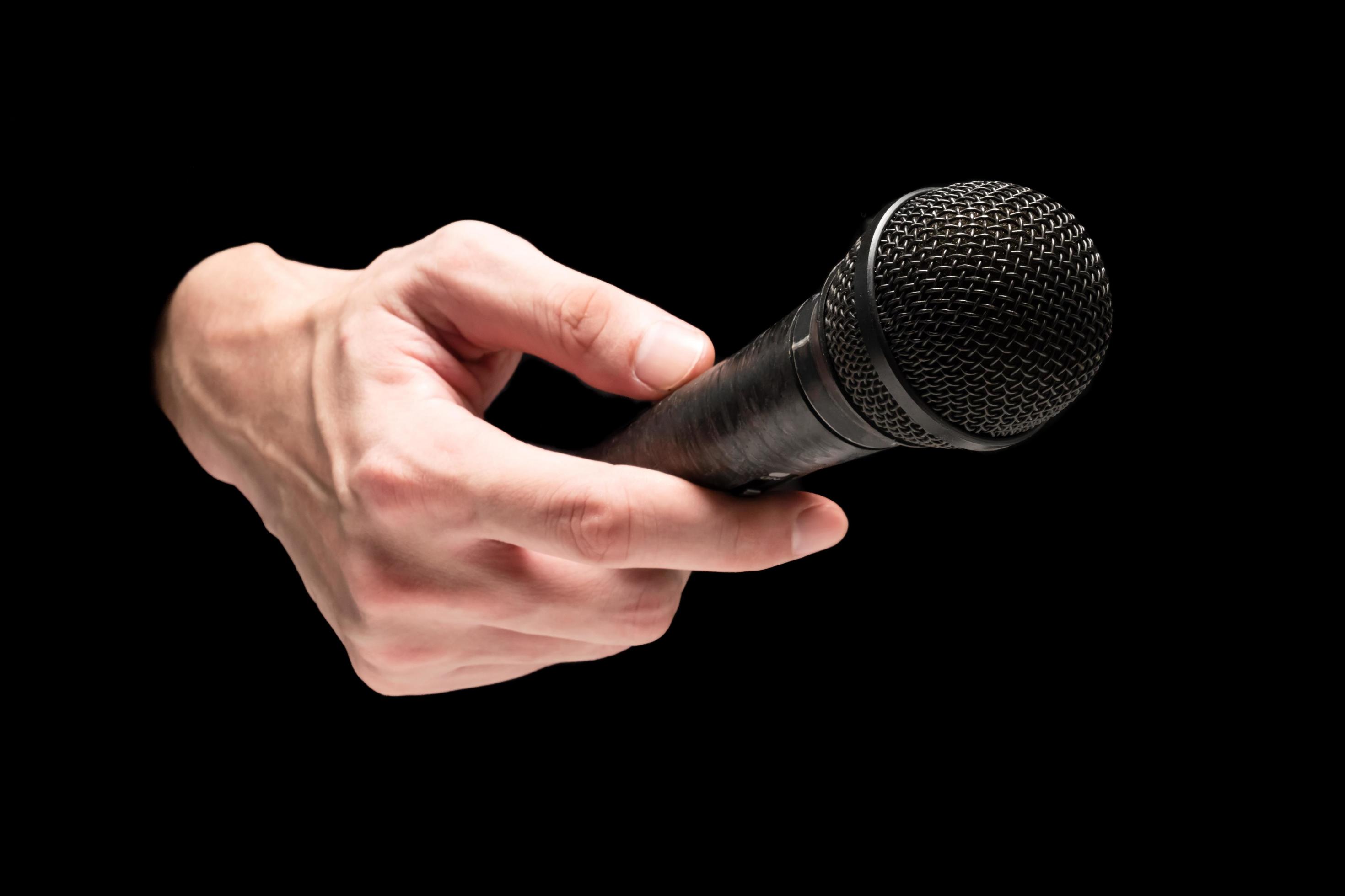 Male hand holding microphone on a black background. 10721862 Stock