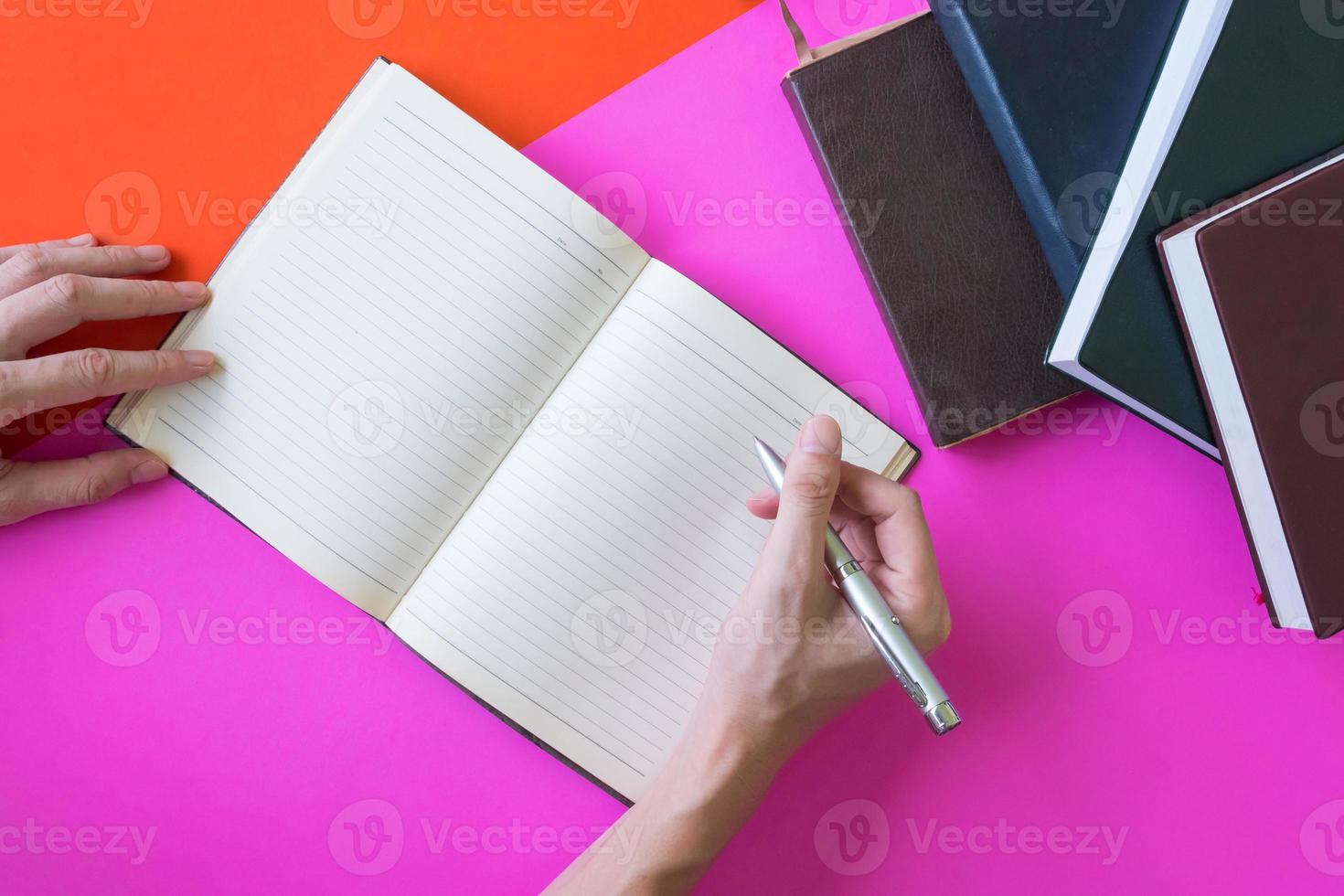 Male hands writing on notebook, hardback book on colorful background photo