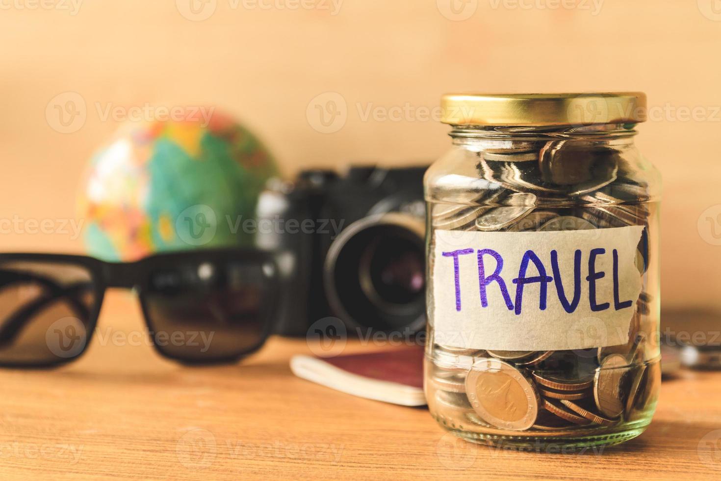 Coins in glass jar with accessories of traveler on wooden table. Saving money for travel concept photo