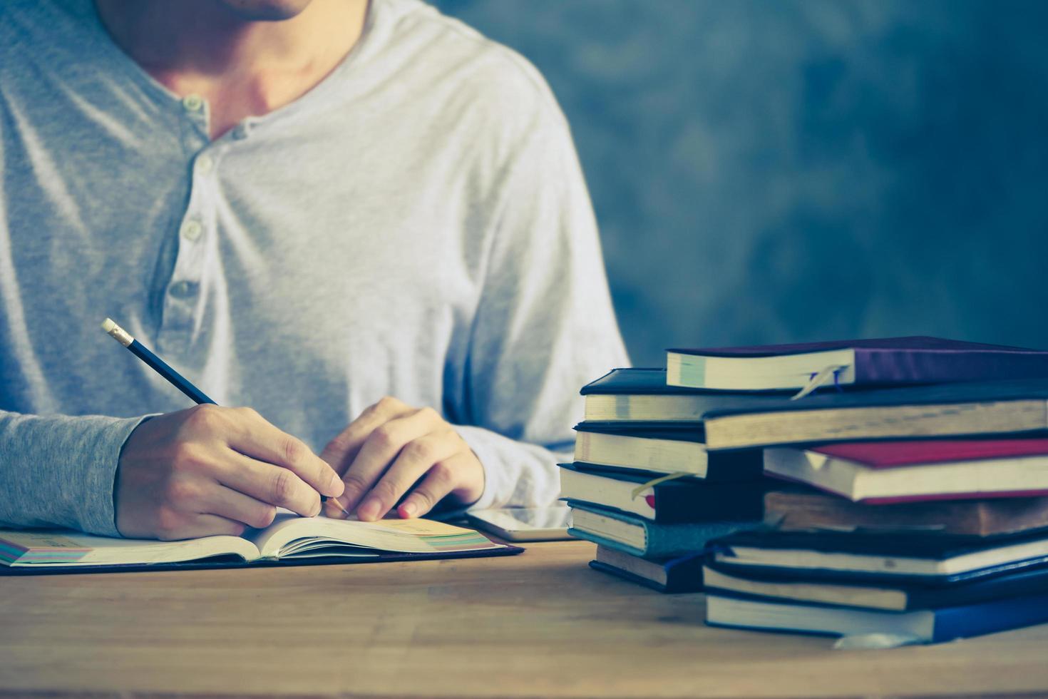 Close up of a man writing in notebook, Stack of old books on wooden desk. Vintage tone photo