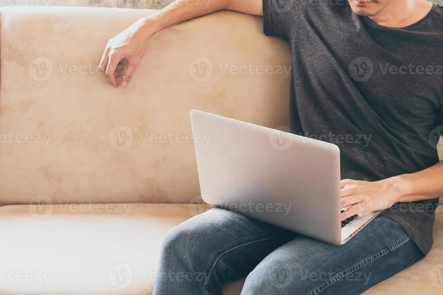 Close up of casual young man sitting on sofa and using a laptop at home. photo