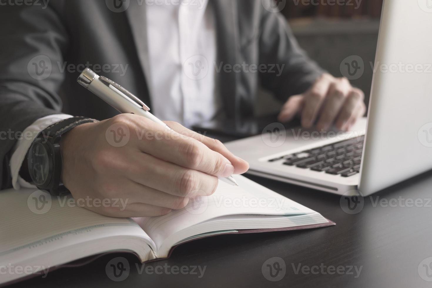 Close up of businessman writing note and using a laptop on the office desk. photo