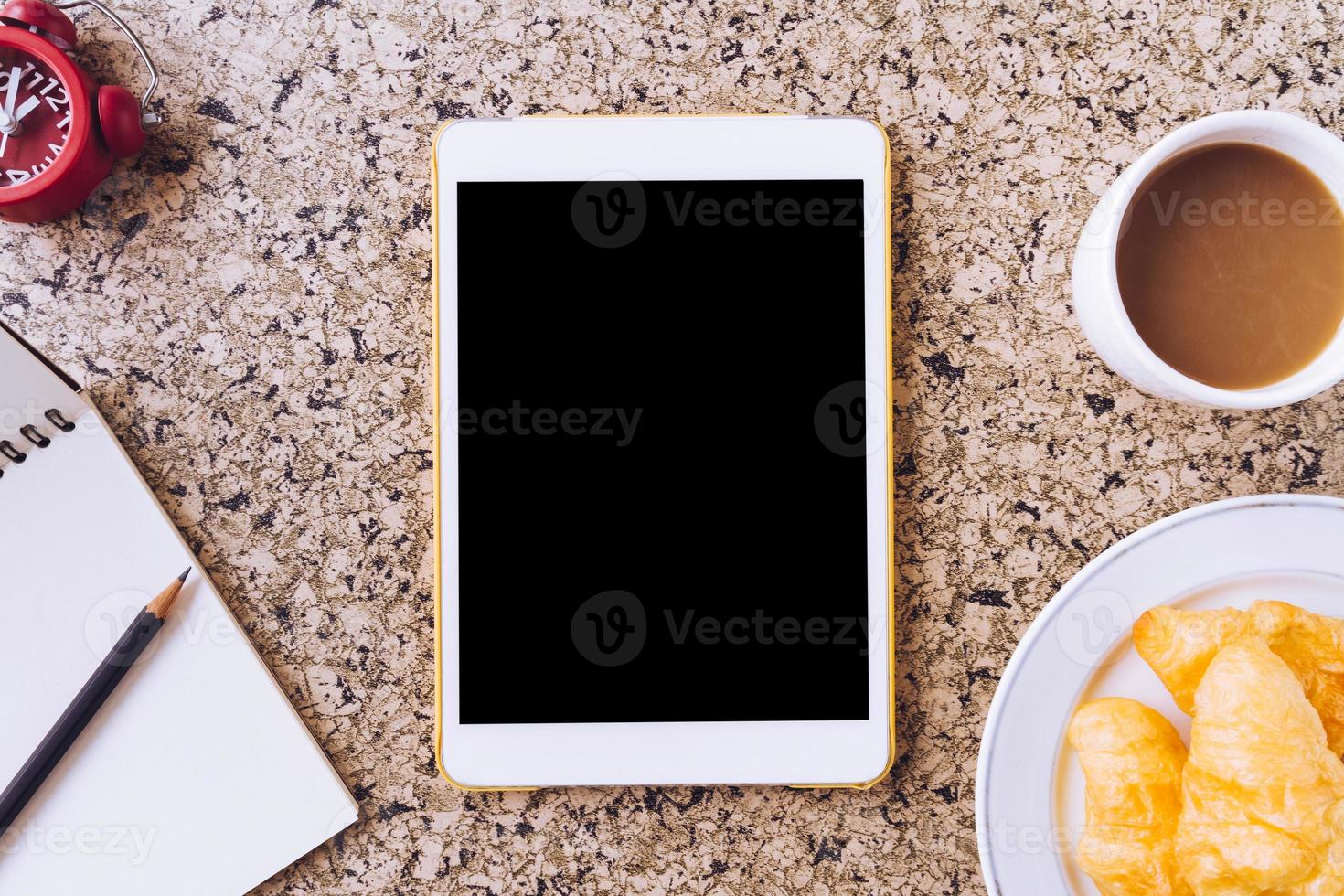 Top view of Tablet with notebook, pencil, clock, coffee and bread on the table photo