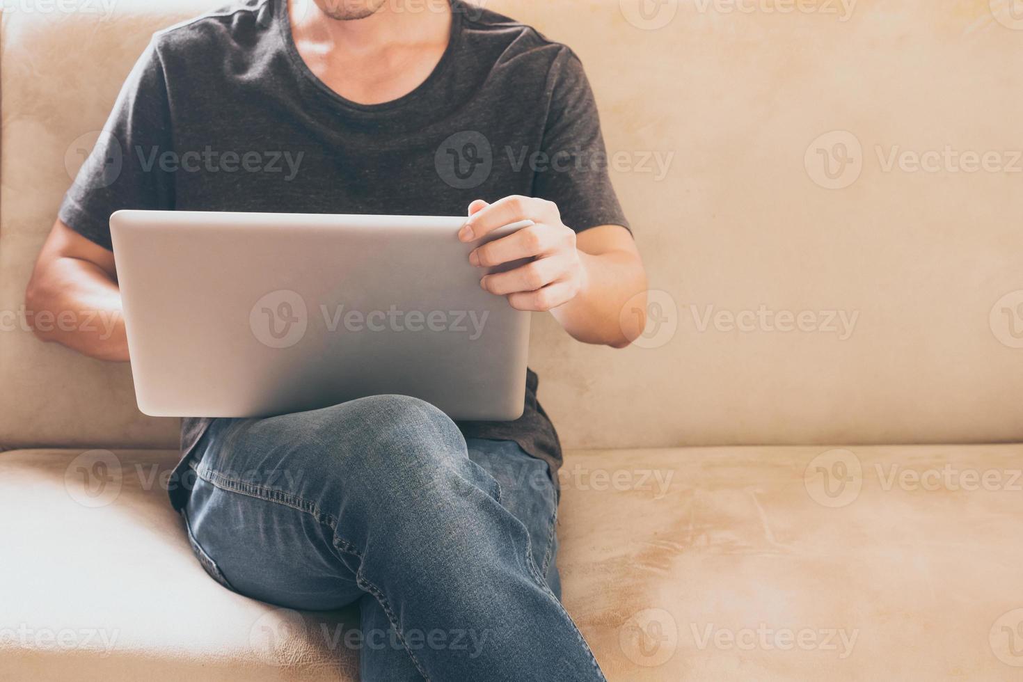 Close up of casual young man sitting on sofa and using a laptop at home. photo