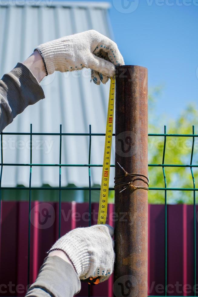 A man measures metal pipes with a tape measure. Construction of the fence. photo