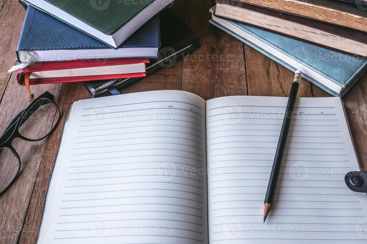 Blank notebook with pencil, glasses and books on wooden table. photo