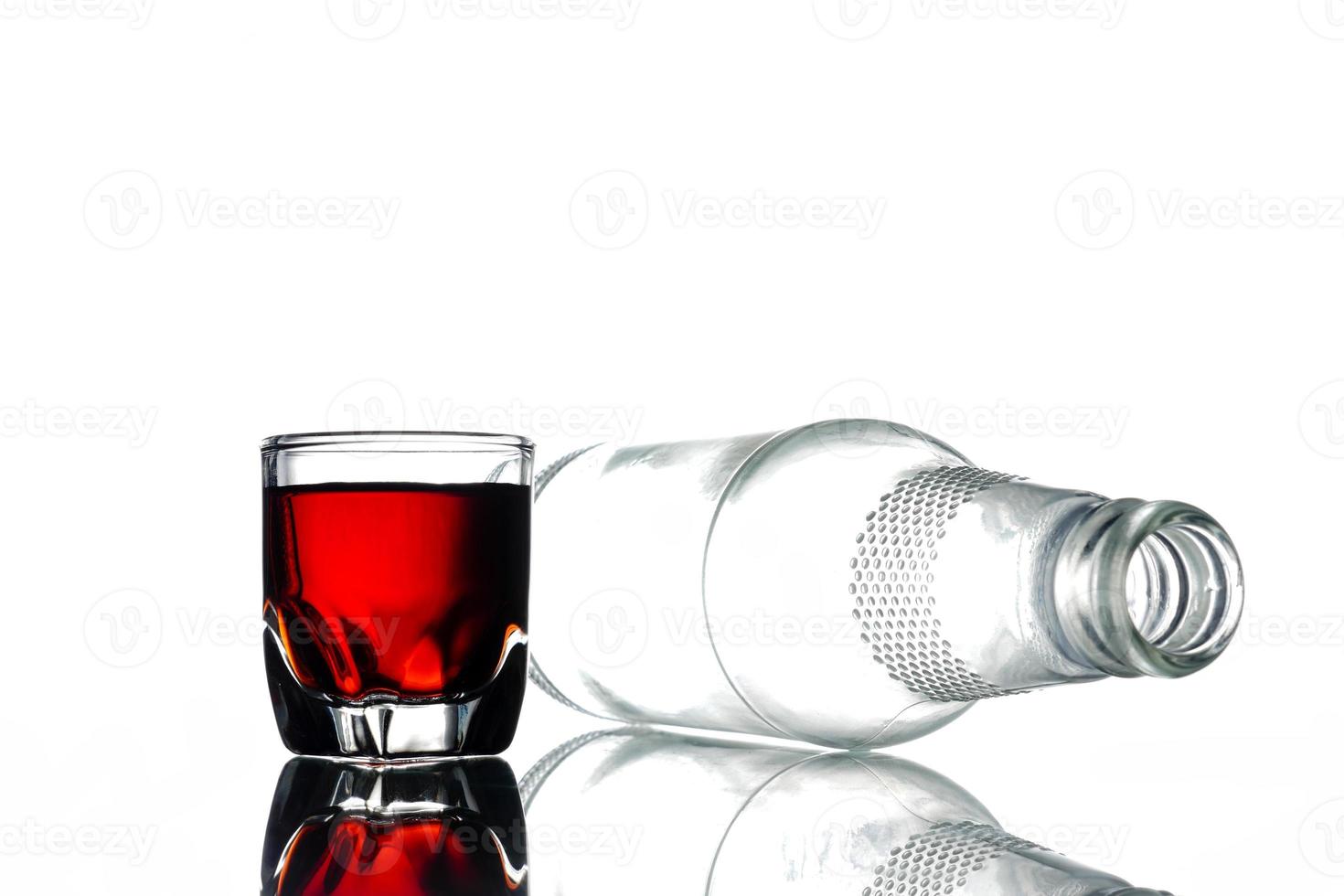 Glass of alcohol and empty bottle on a white background. photo