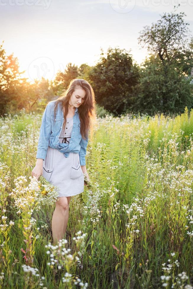 Beautiful girl  walking on field on summer with wildflowers. photo