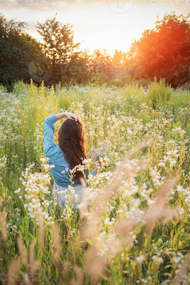 hermosa chica caminando en el campo en verano con flores silvestres. foto
