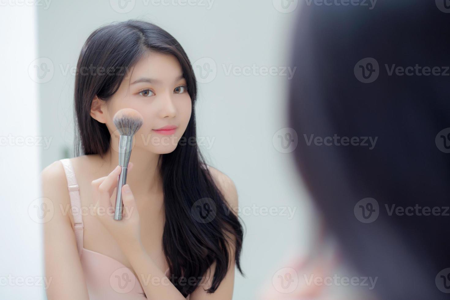 Beauty portrait young asian woman smiling with face looking mirror applying make up with blusher cheek in the room, happy beautiful girl blush applying facial, skin care and cosmetic concept. photo