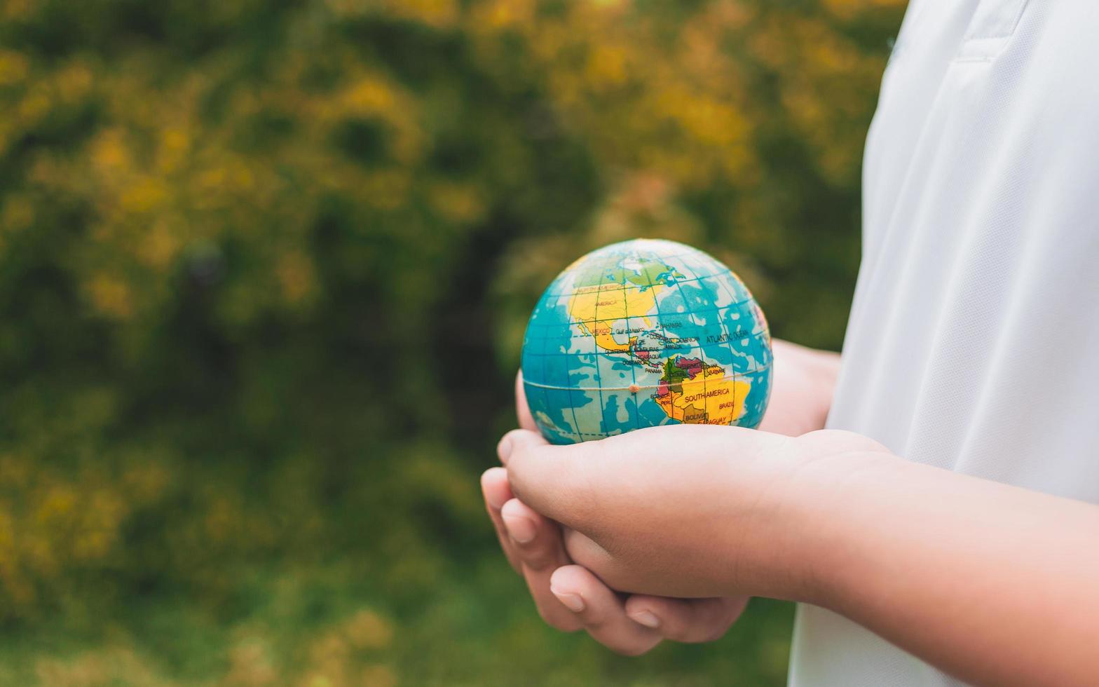 Planet earth in the boy's hands saves and protects the world over blurred green nature background. Environmental concept on Earth Day. photo