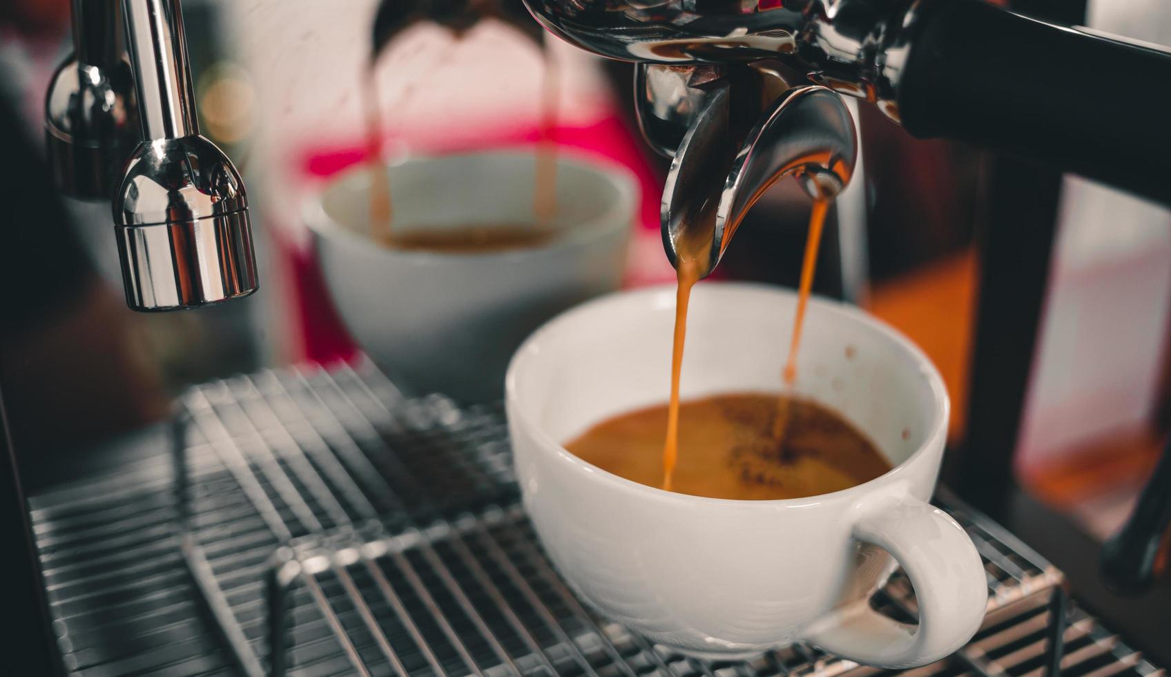 el primer plano del espresso que sale de la máquina de café que fluye hacia la taza de café prepara café para los clientes en la cafetería. foto