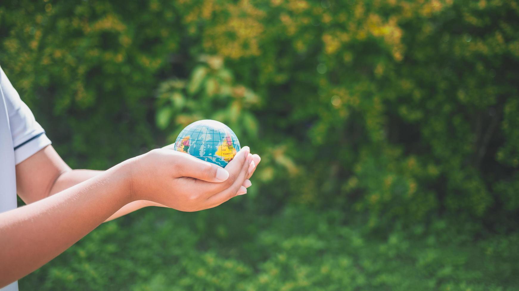 Planet earth in the boy's hands saves and protects the world over blurred green nature background. Environmental concept on Earth Day. photo