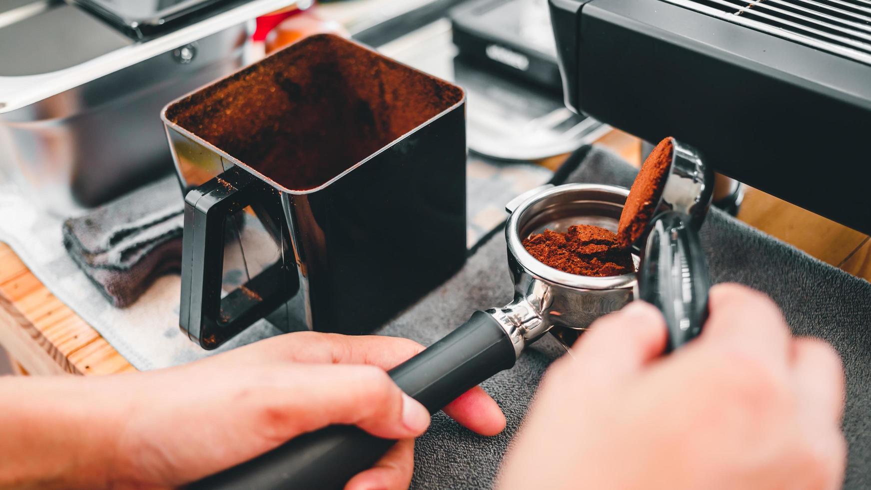 Close-up barista pouring freshly ground coffee beans in a portafilter by the coffee grinder to make coffee for customers in the cafe photo