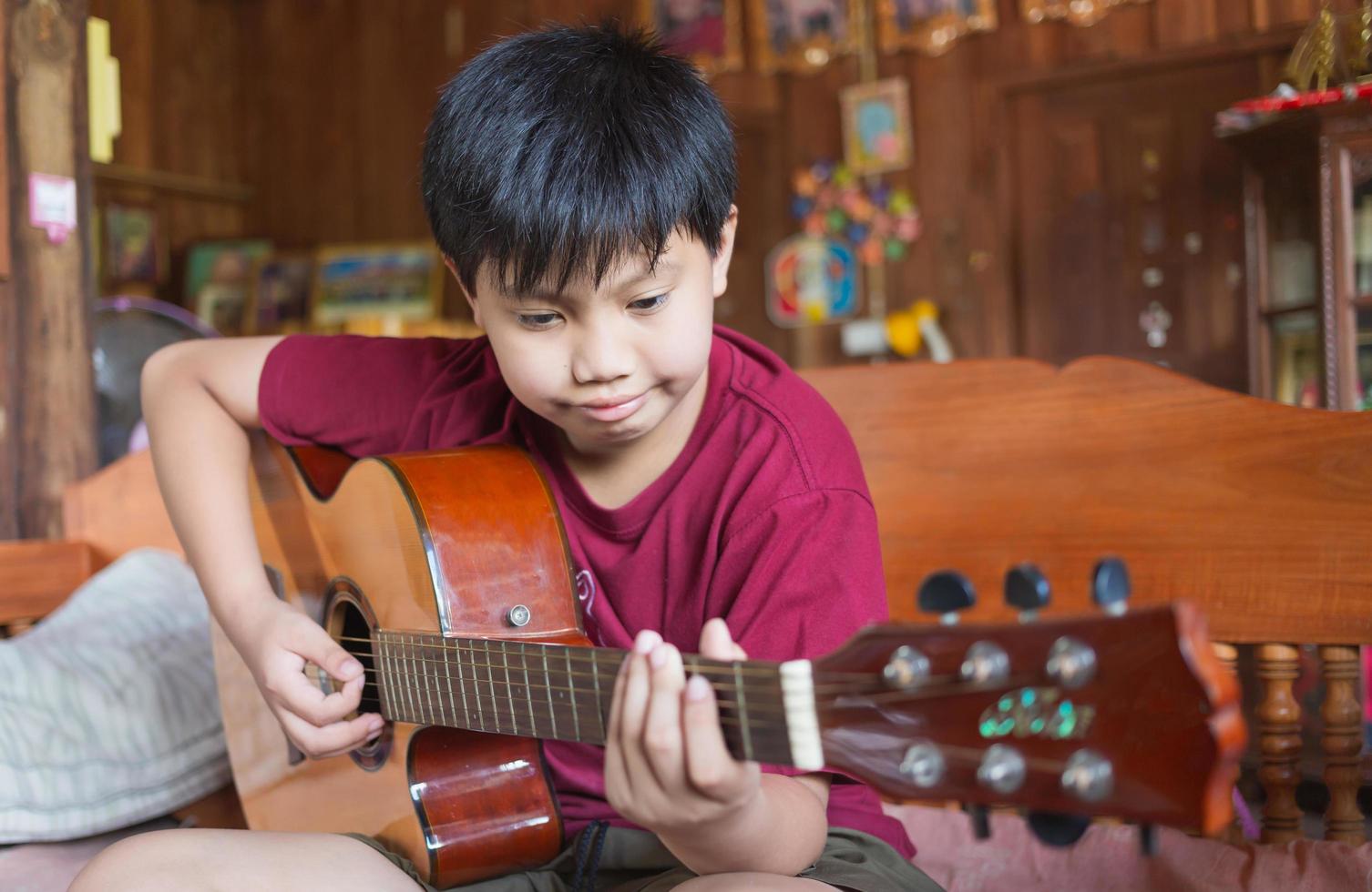 A cute Asian boy wearing headphones video calls learning  music and writing songs online on his computer laptop using an acoustic guitar happily at home kid creators concept photo
