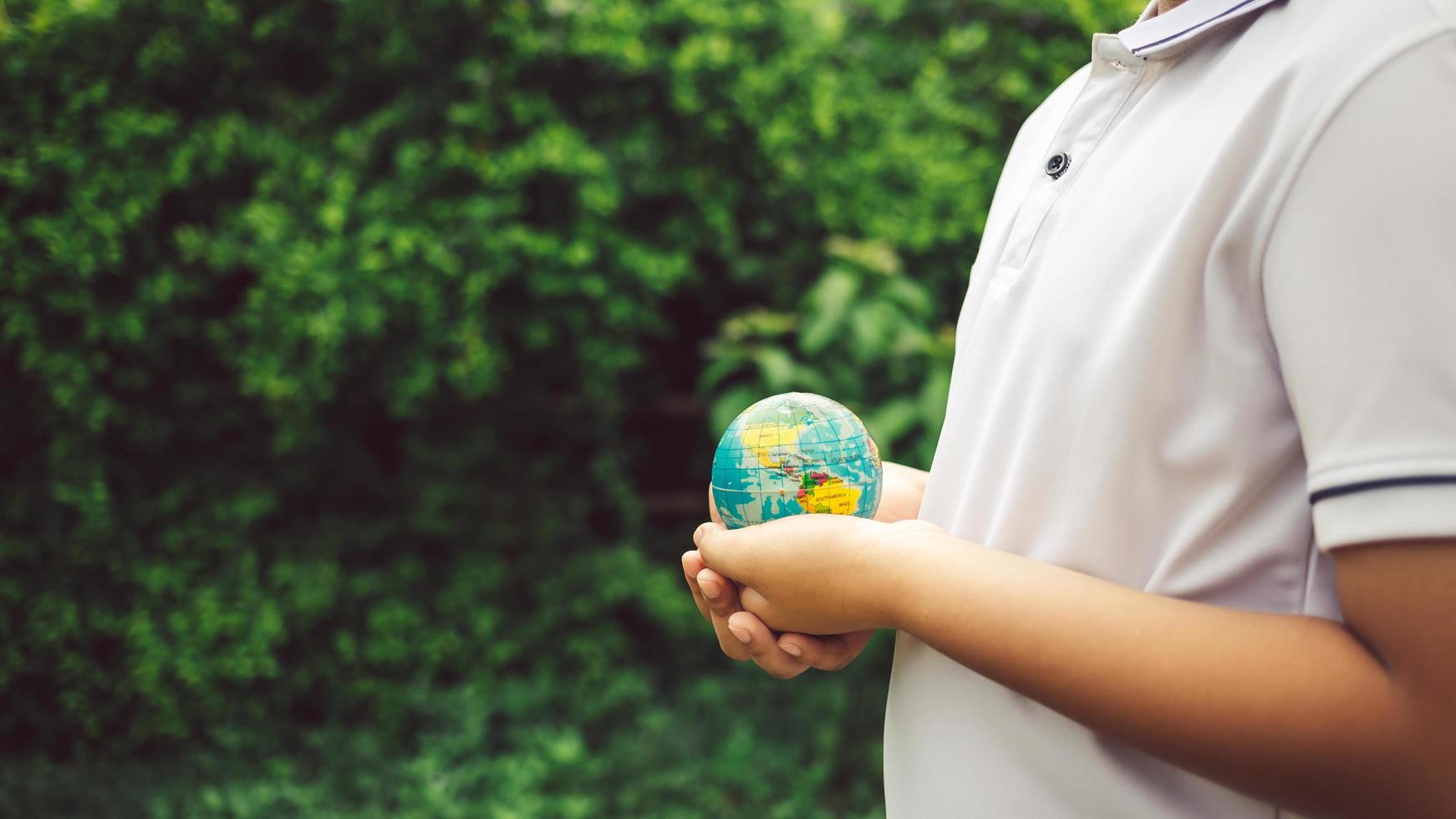 Planet earth in the boy's hands saves and protects the world over blurred green nature background. Environmental concept on Earth Day. photo