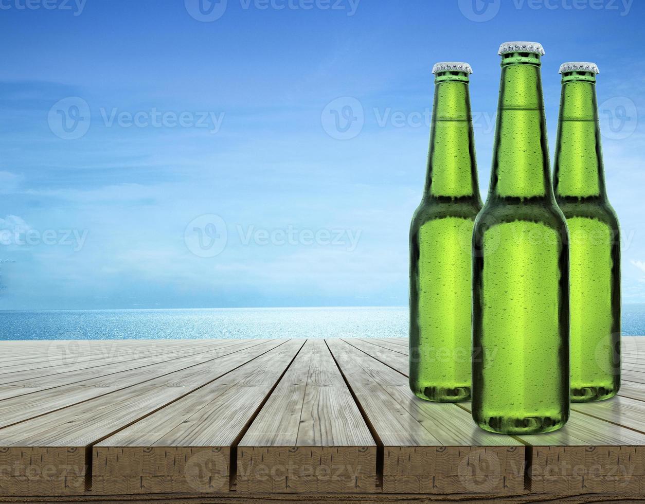 botella de cerveza con gotas de agua en la parte superior de la mesa de madera índigo y los productos de fondo azul se pueden colocar o cortar para mostrar - concepto, playa y verano foto