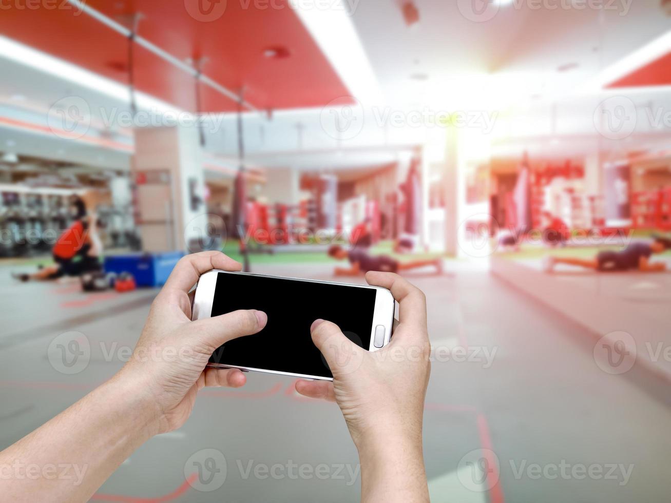 hand holding mobile smart phone with blur fitness gym equipment background photo