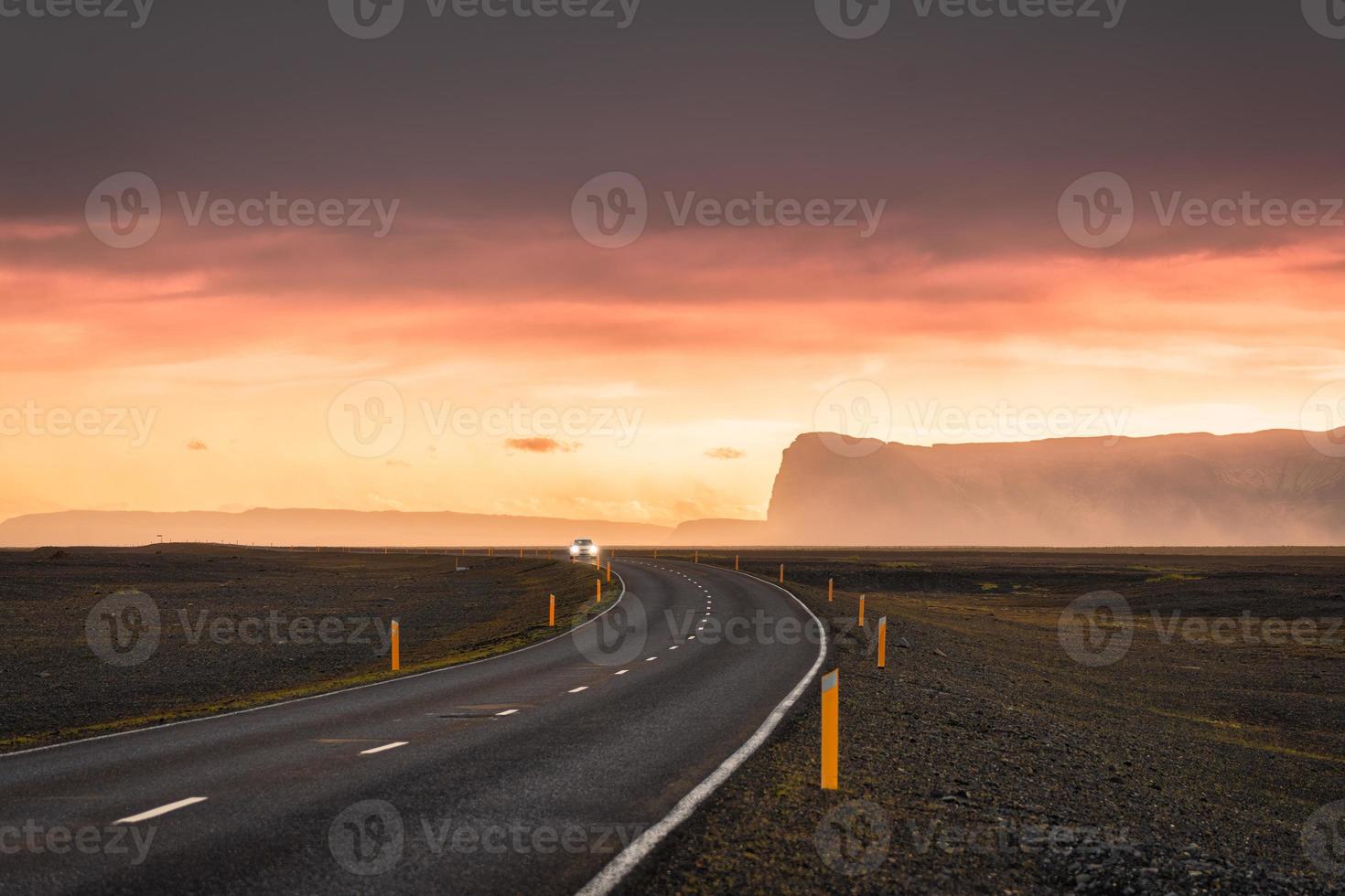 Scenic curved asphalt road with car driving and sunset sky on mountain at Iceland photo