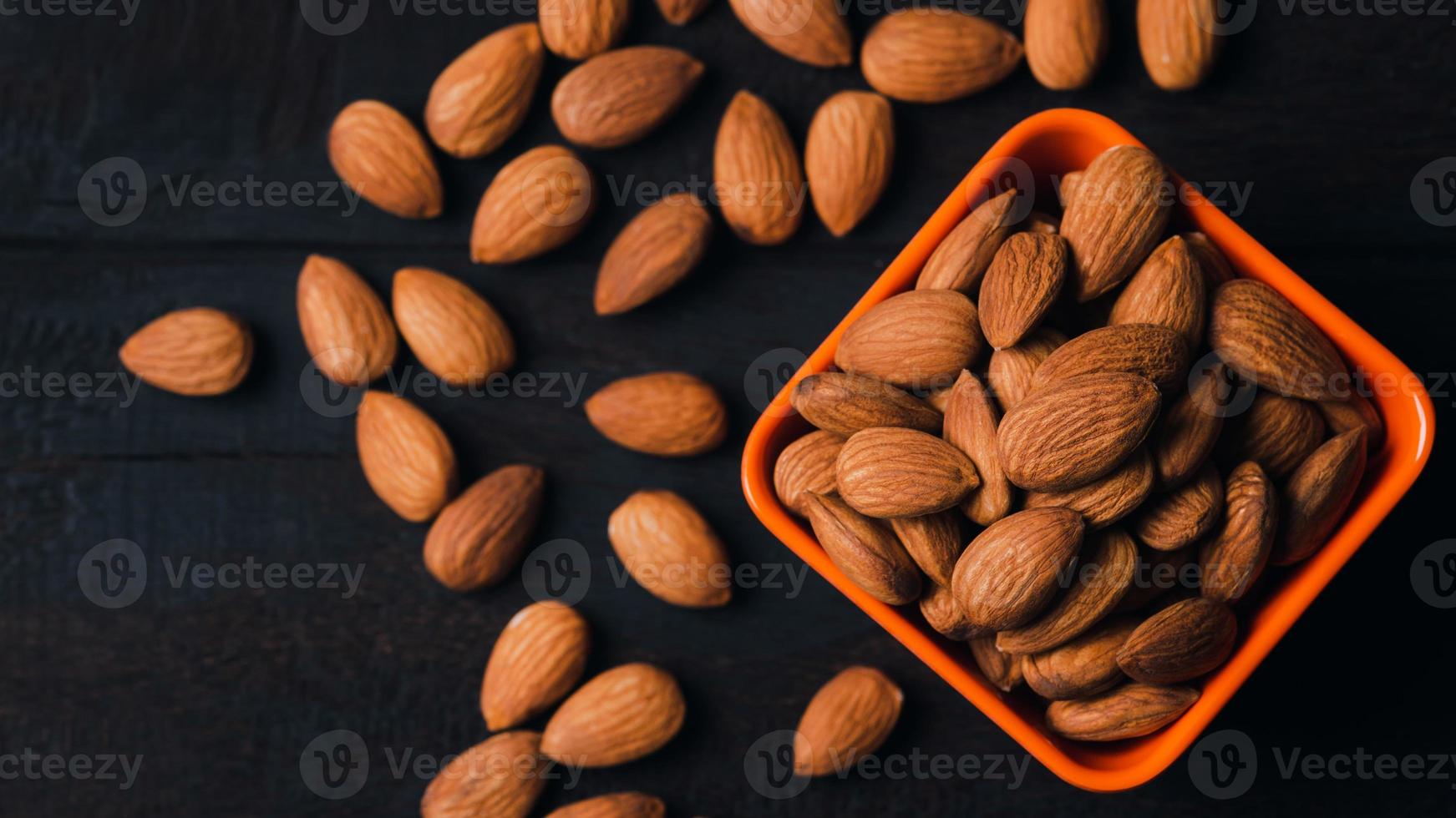 Almonds in an orange cup and placed on an old wooden table, closeup