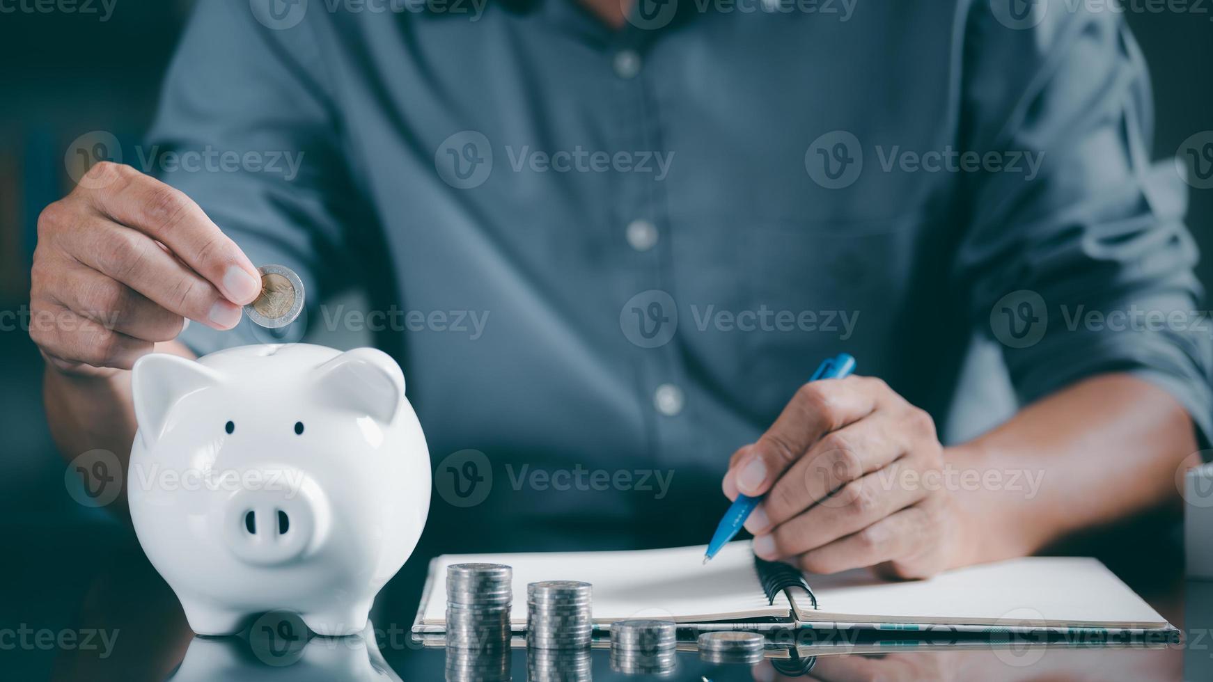 A young man puts coins in a piggy bank to save and record his growth in accounting, finance and investment ideas for planning and managing his retirement savings. photo