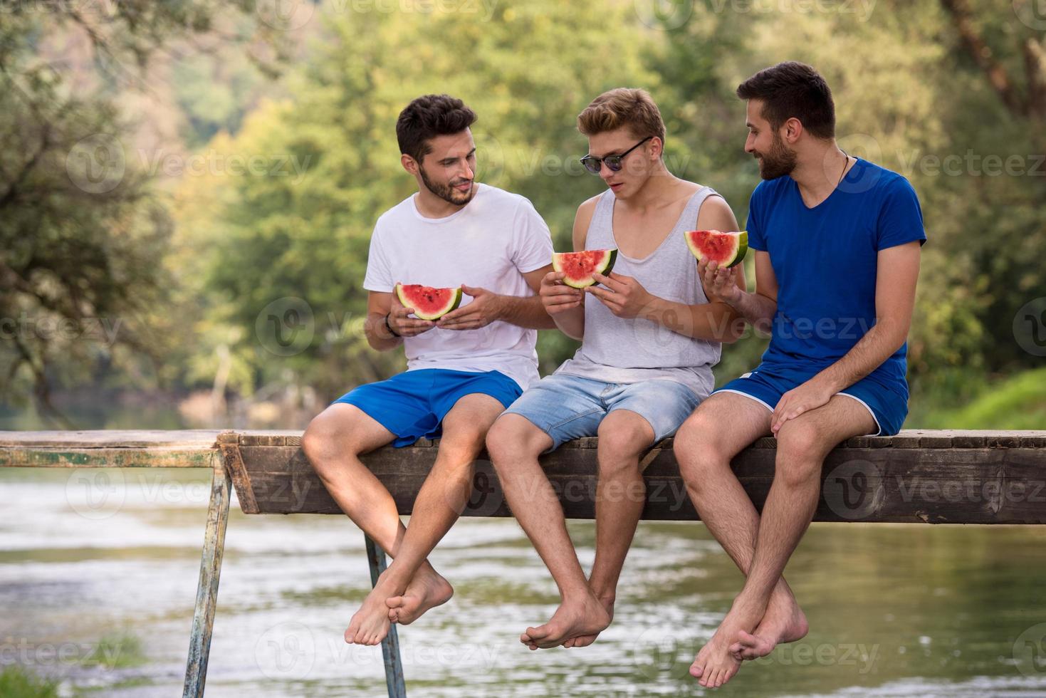 men enjoying watermelon while sitting on the wooden bridge photo