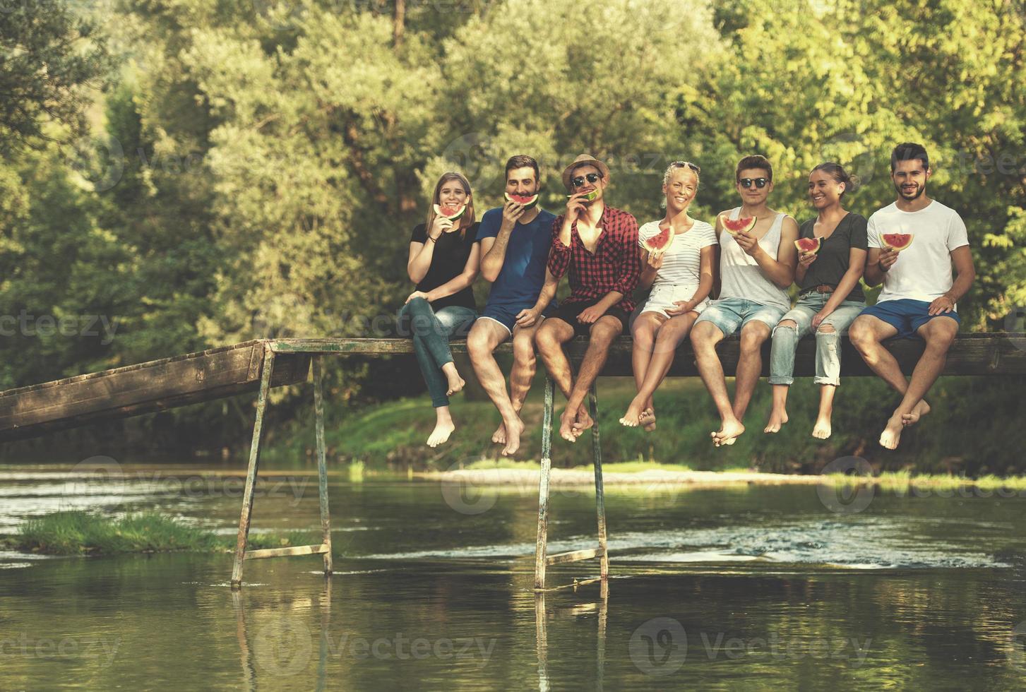 friends enjoying watermelon while sitting on the wooden bridge photo