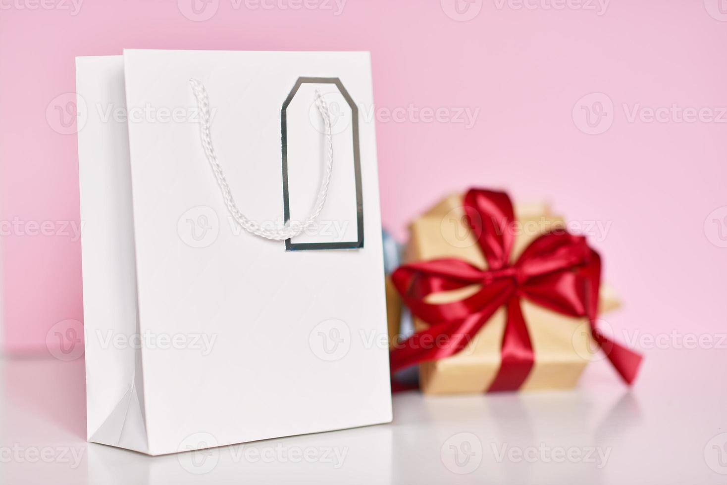 caja de regalo con cinta y bolsa de papel sobre un fondo rosa foto