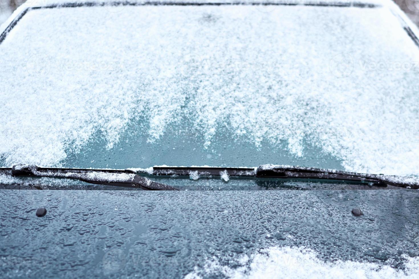 Close up of car windshield and wipers covered with ice and snow on winter day photo