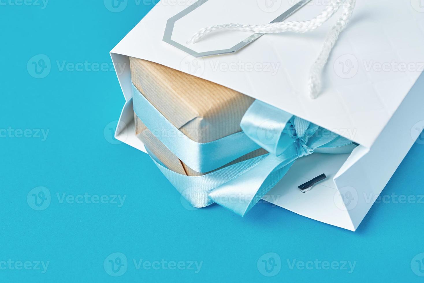 White shopping bag with gift box on blue background, top view photo