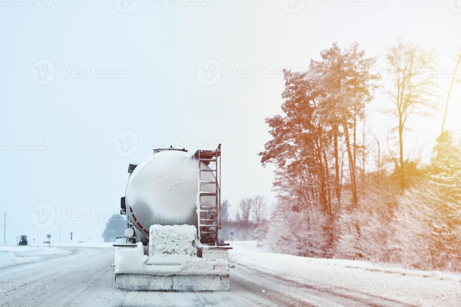 Truck with cargo tank on slippery snow winter road outside the city, back view photo