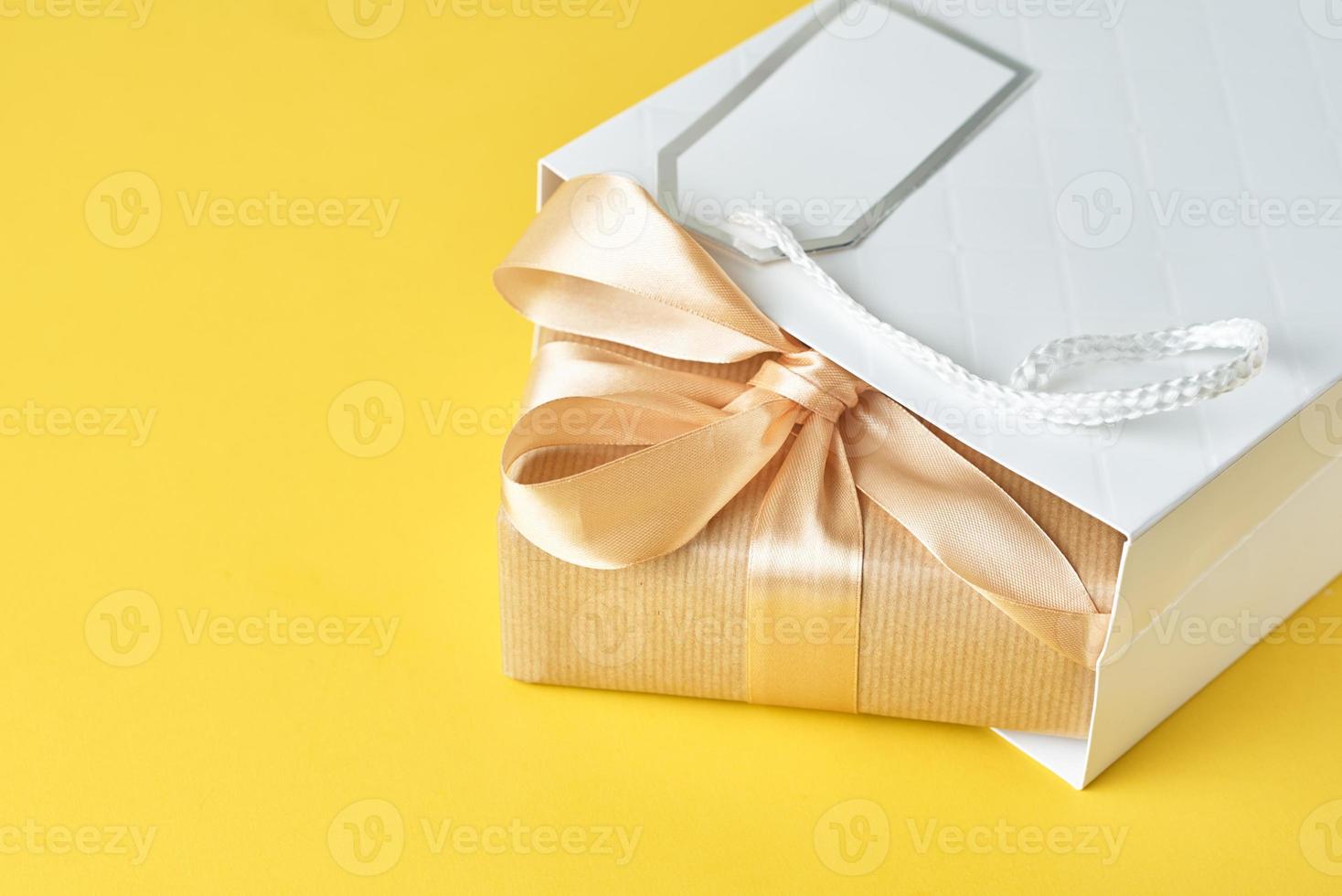 White shopping bag with gift box on yellow background, top view photo