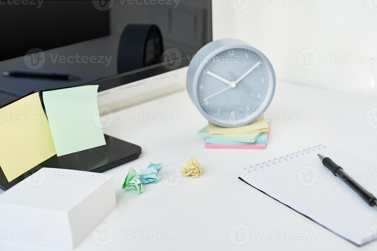 lugar de trabajo con reloj, suministros de oficina y notas adhesivas foto