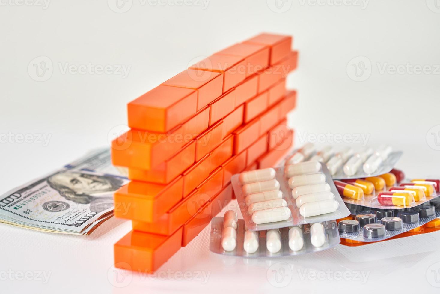 píldoras médicas y billetes de dólar dinero separado con una pared de ladrillos de juguete foto