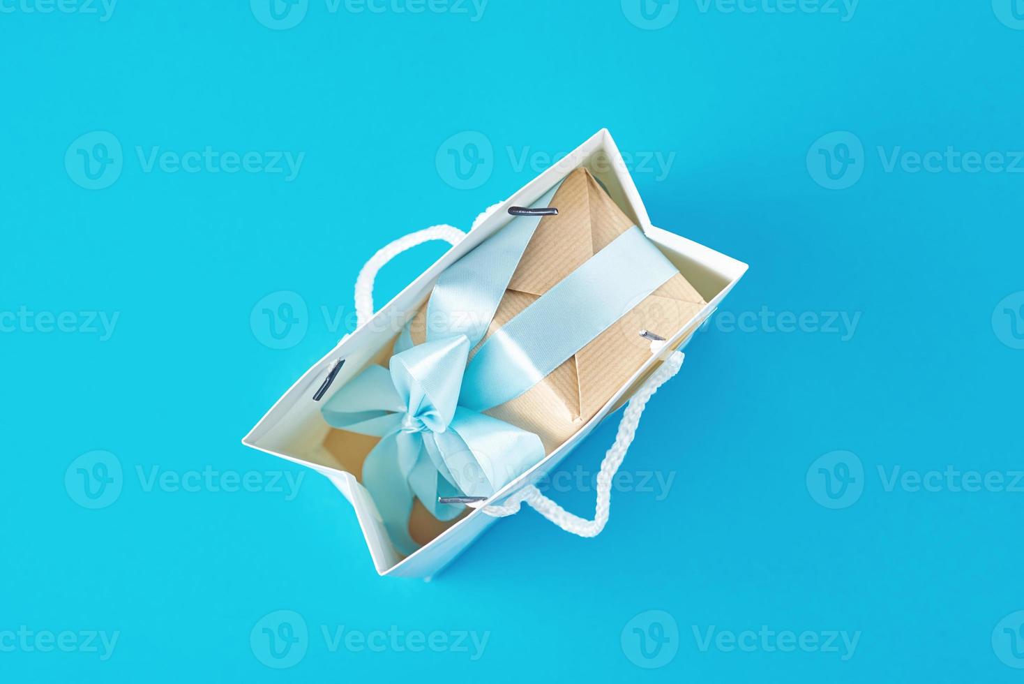 Top view inside open red paper shopping bag wirh gift box on blue background. photo