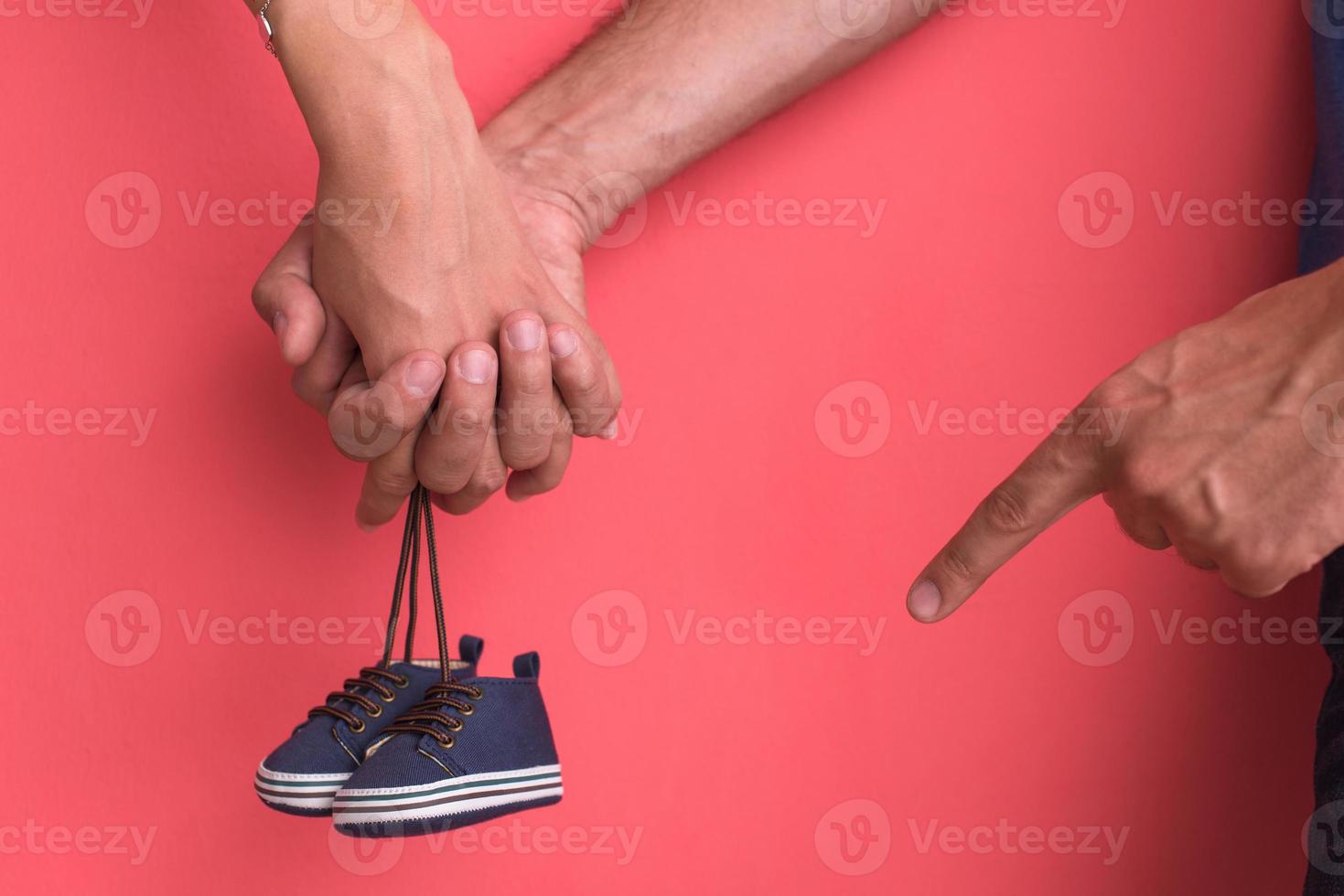 young pregnant couple holding newborn baby shoes photo