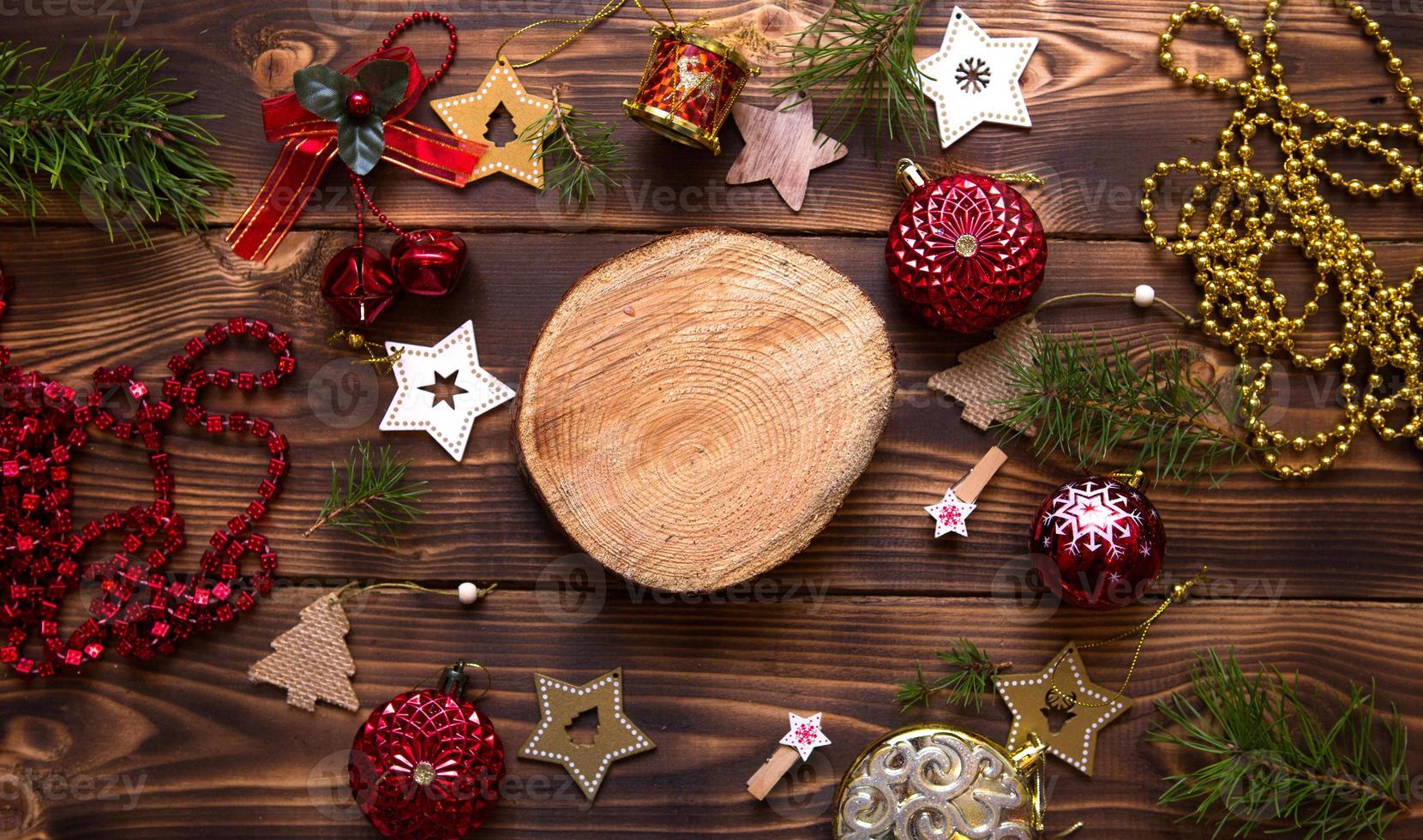 Christmas flat lay of red balloons and wooden stars and clothespins on a dark background with tree trunk section for notes in center. New year's frame, space for text. Xmas toys, beads, pine branches photo